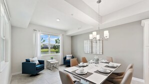 A modern dining area with a large table set for six, a blue sofa, and a view of the outdoors through a large window.