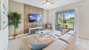 A modern living room with a flat-screen TV, a large window, and a ceiling fan.