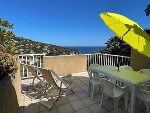 Een balkon met een tafel en stoelen, een gele parasol en uitzicht op zee en heuvels.