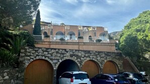 Um edifício com arco de pedra na entrada, varanda e área de estacionamento com carros.