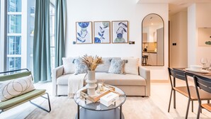 Ein modernes Wohnzimmer mit Sofa, Couchtisch und Essbereich. Drei gerahmte Kunstwerke sind an der Wand zu sehen, eine Vase mit getrockneten Pflanzen und ein Blick in die Küche durch einen Bogen.