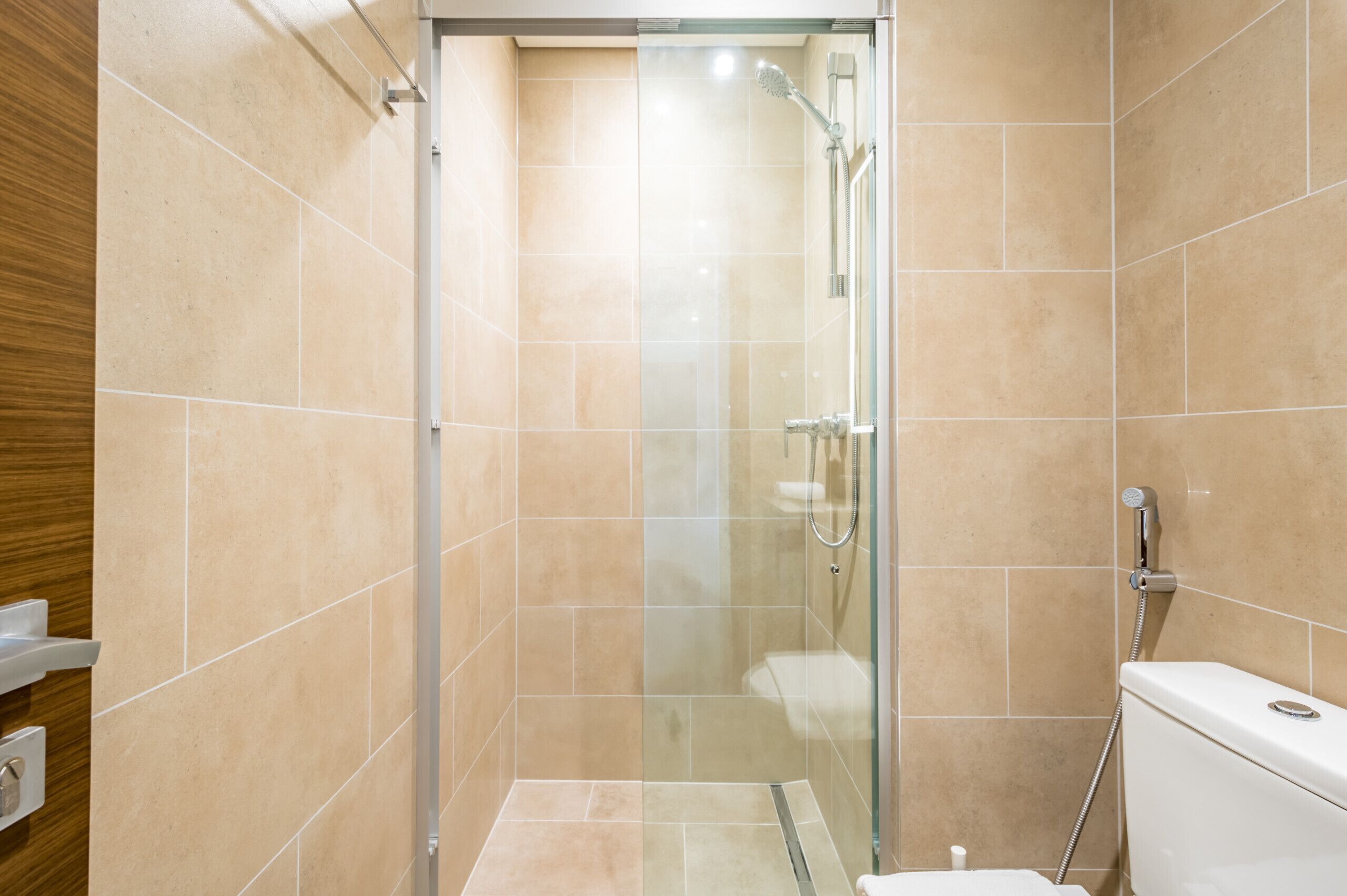 A modern bathroom with a glass-enclosed shower, beige tiles, and a white toilet.