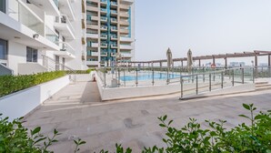 Un immeuble d’appartements moderne doté d’une piscine sur le toit, comprenant une rambarde en verre et un espace salon extérieur.