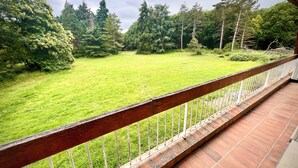 Un balcon donnant sur une cour verdoyante et des arbres.