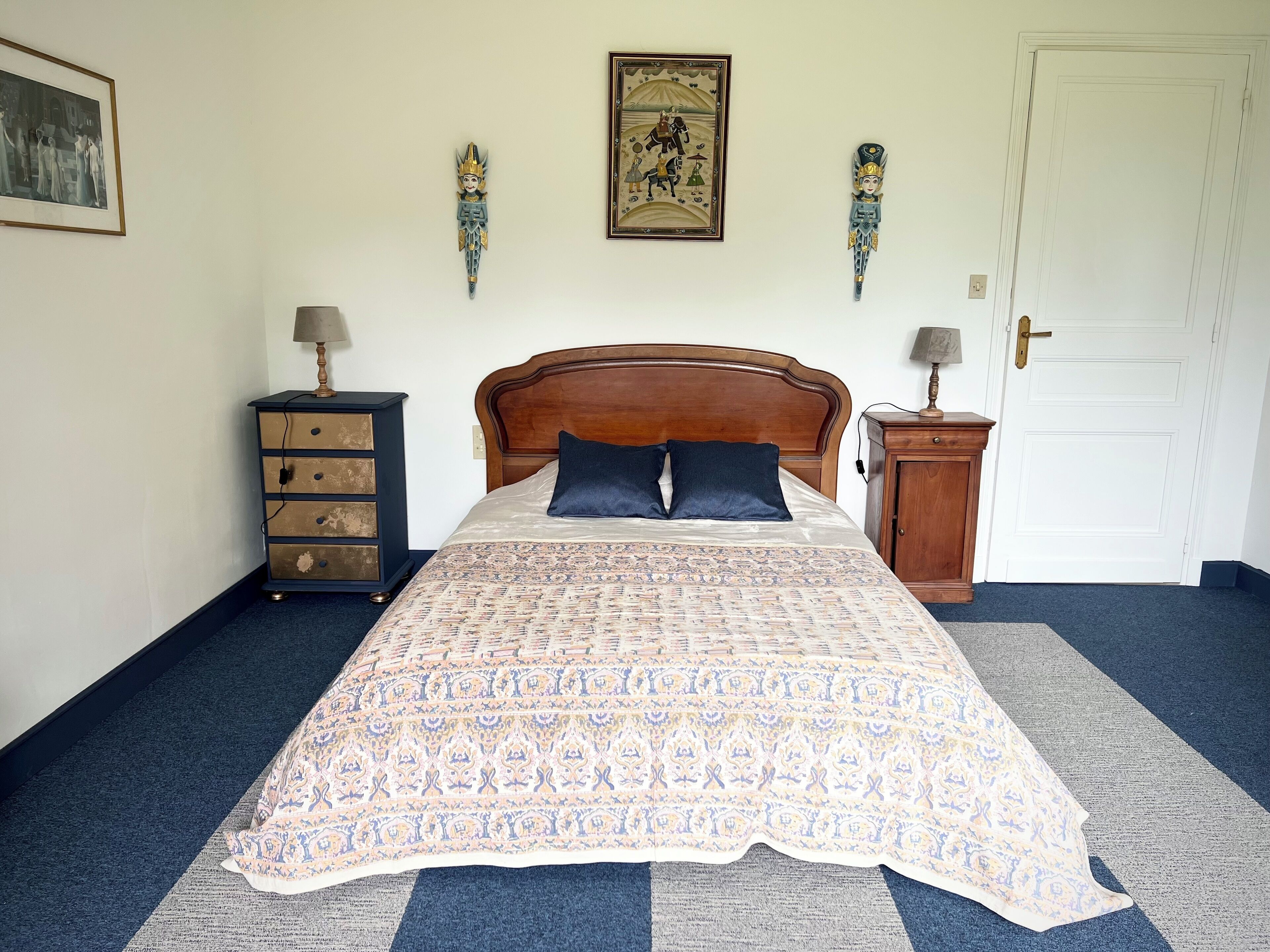 Een slaapkamer met een houten bed, twee wandlampen, een ingelijst kunstwerk en een nachtkastje met een lamp.