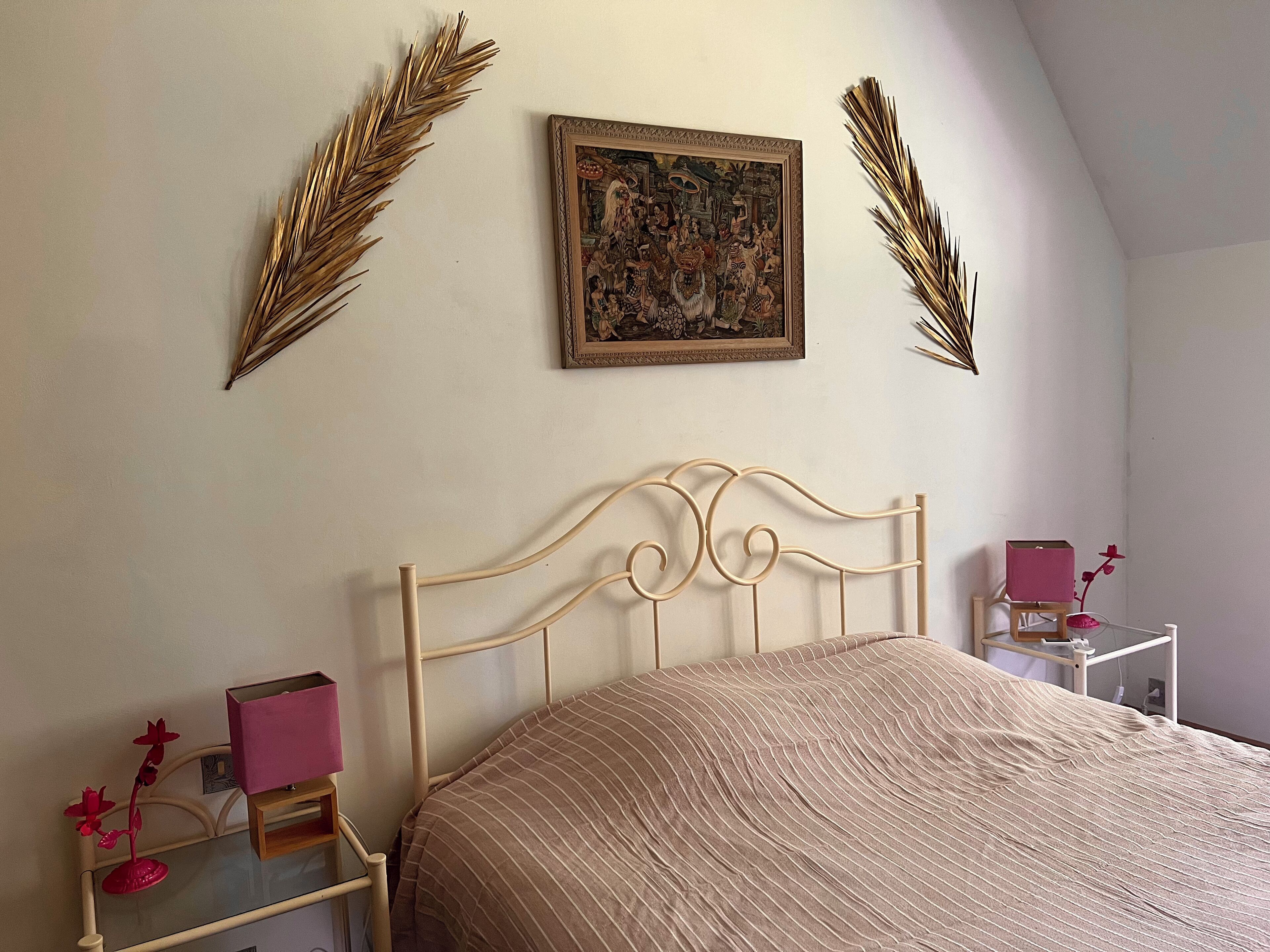 A bedroom with a bed, a nightstand, a lamp, a picture frame, and decorative leaves.