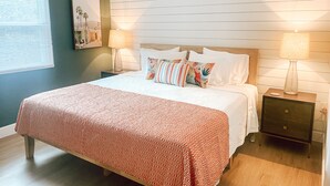 Un dormitorio con una cama, dos mesitas de noche, una lámpara de pared y un cuadro enmarcado.