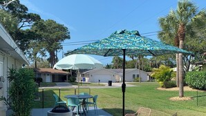 Un espacio de patio con mobiliario exterior, un paraguas estampado y césped.