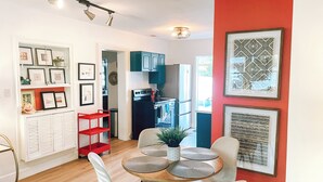 Una cocina moderna con refrigerador, estufa y armarios. Hay un comedor con mesa y sillas, y una pared de acento roja.
