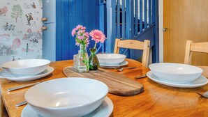 Una mesa de comedor con cuencos blancos, una tabla de cortar de madera y dos jarrones con flores rosas.
