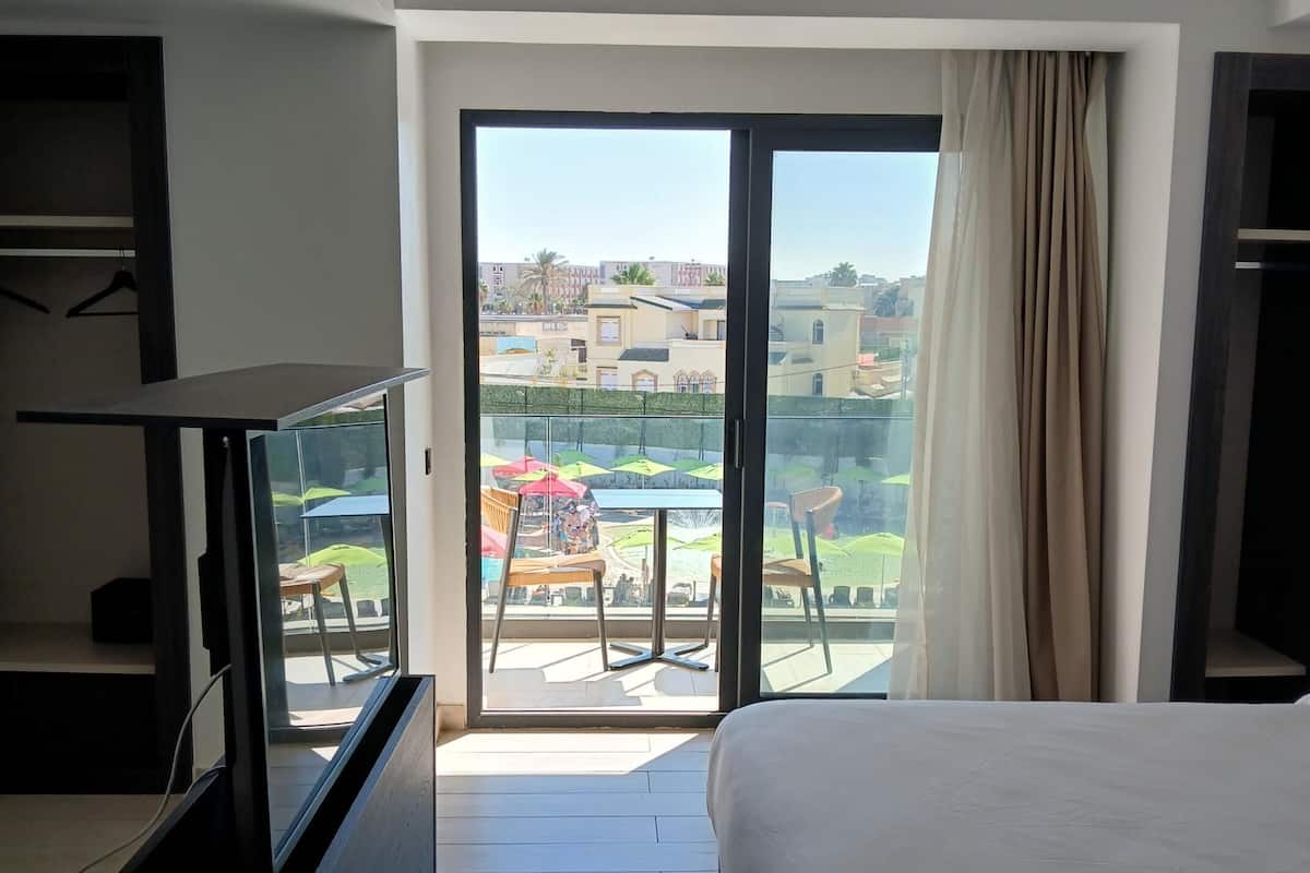 A hotel room with a large bed, a television, and a balcony with outdoor seating.