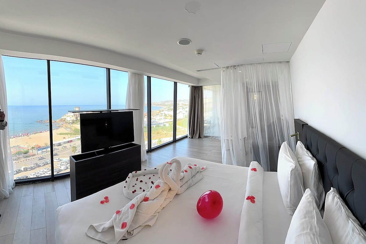 A modern hotel room with a large bed, a flat-screen TV, and a view of the beach.