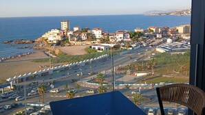 A balcony with a view of a coastal town, a parking area, and a table with chairs.