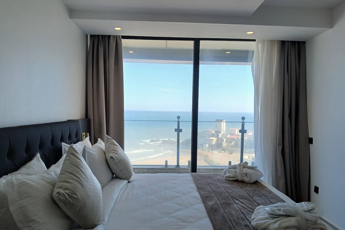 A hotel room with a large bed, a view of the beach, and a balcony with a railing.