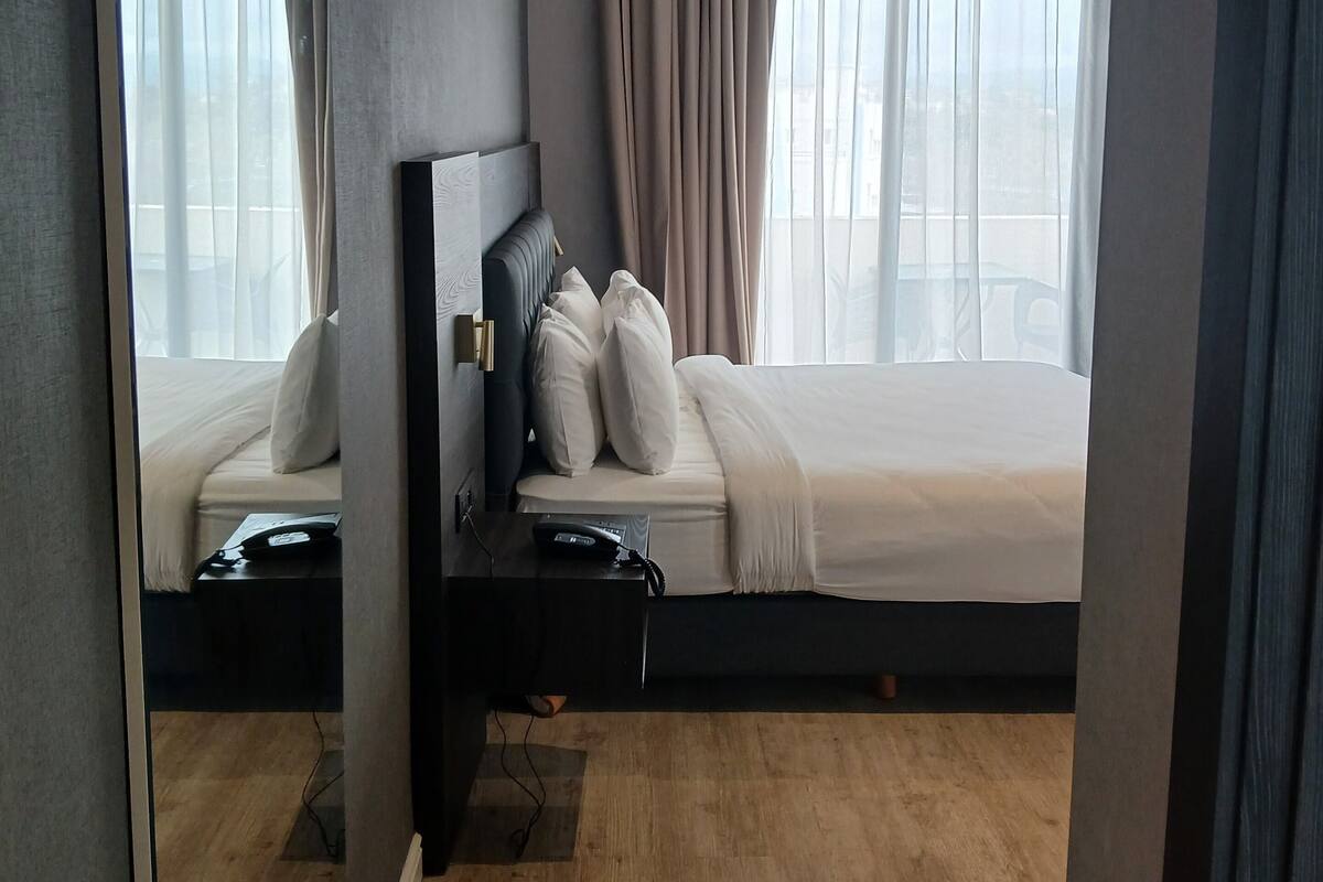 A modern hotel room with a large bed, a bedside table with a phone, and a mirror.