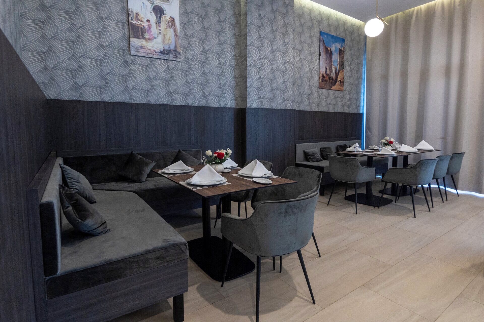 Um restaurante moderno com parede revestida em madeira escura, assentos estofados em cinza e mesa de madeira posta para refeição.