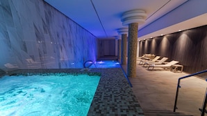 A spa area with a hot tub, lounge chairs, and a wall with a water feature.