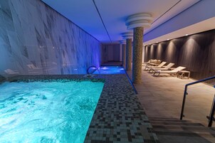 A spa area with a hot tub, lounge chairs, and a wall with a water feature.