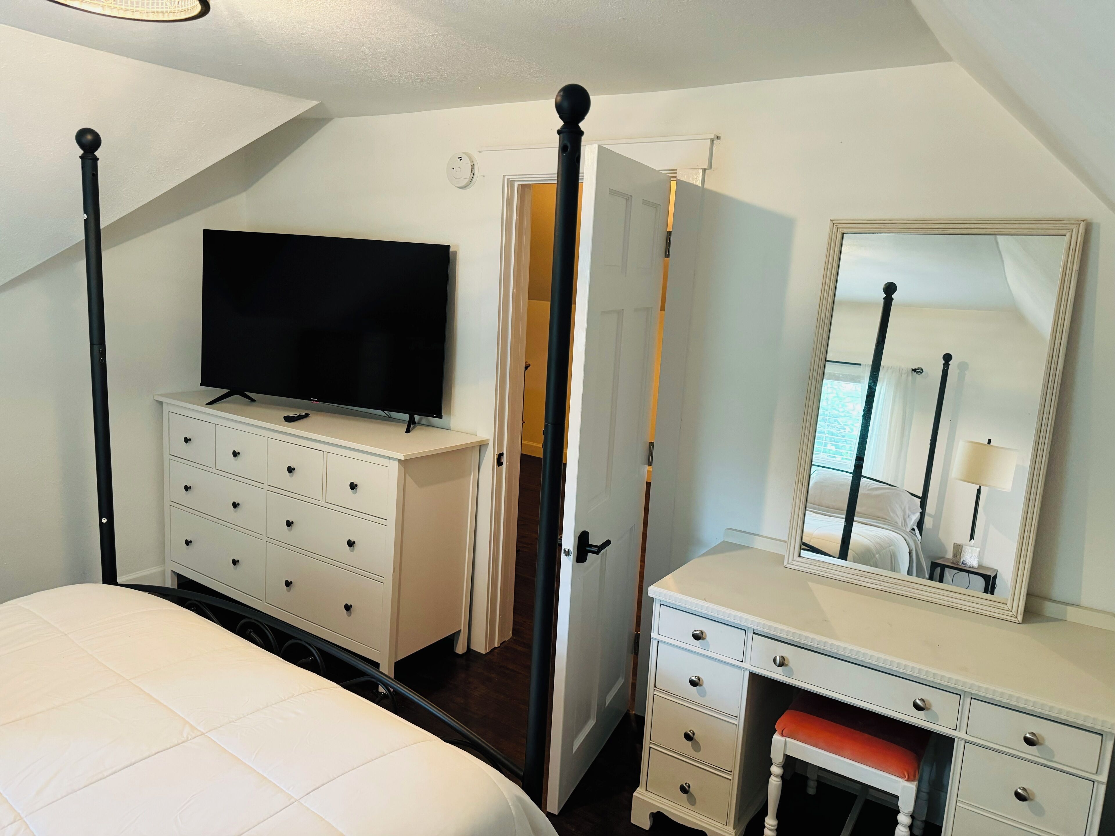 A bedroom with a bed, a dresser, a television, a mirror, and a door leading to another room.