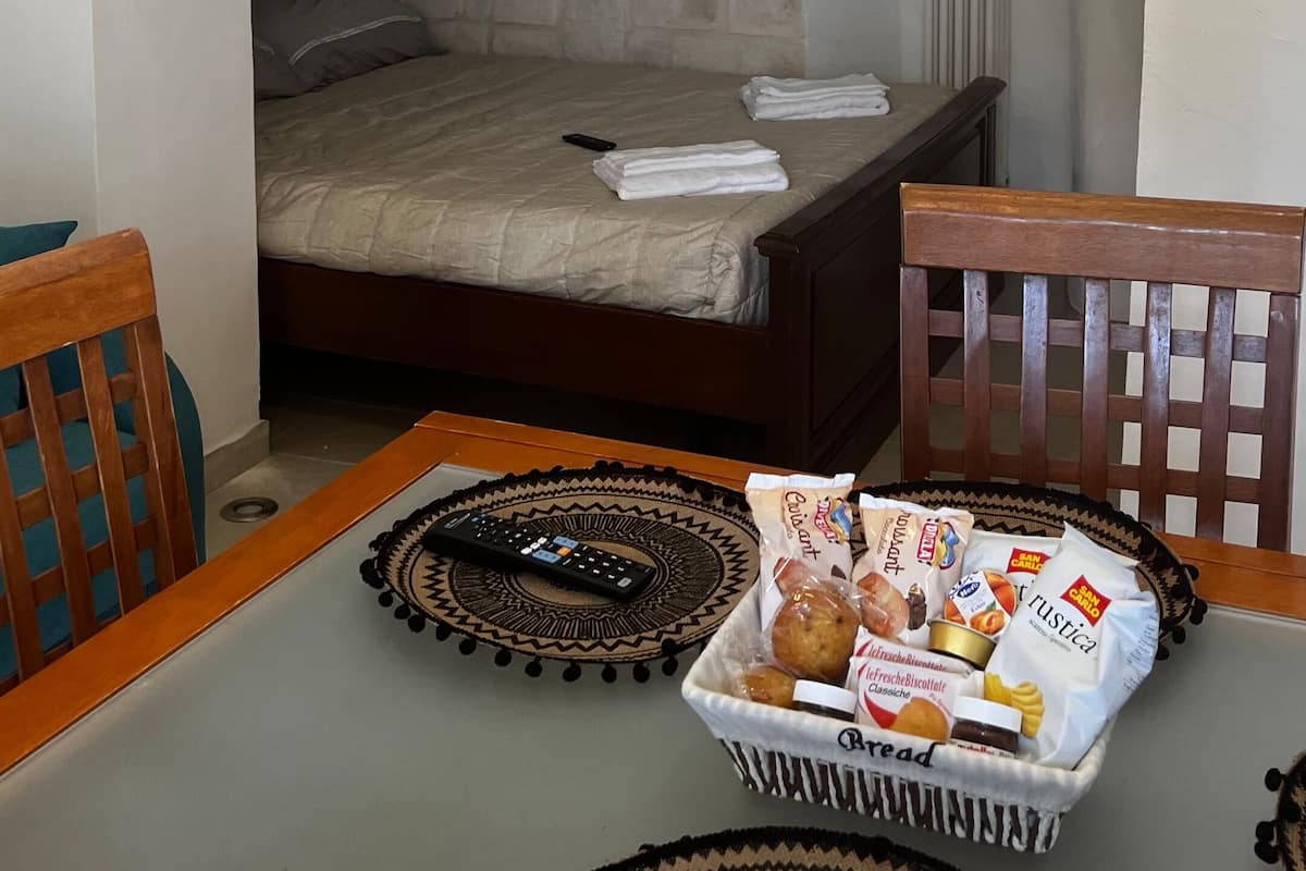 Una habitación acogedora con un arco de piedra que lleva a una cama, una mesa con una cesta de pan y un control remoto.