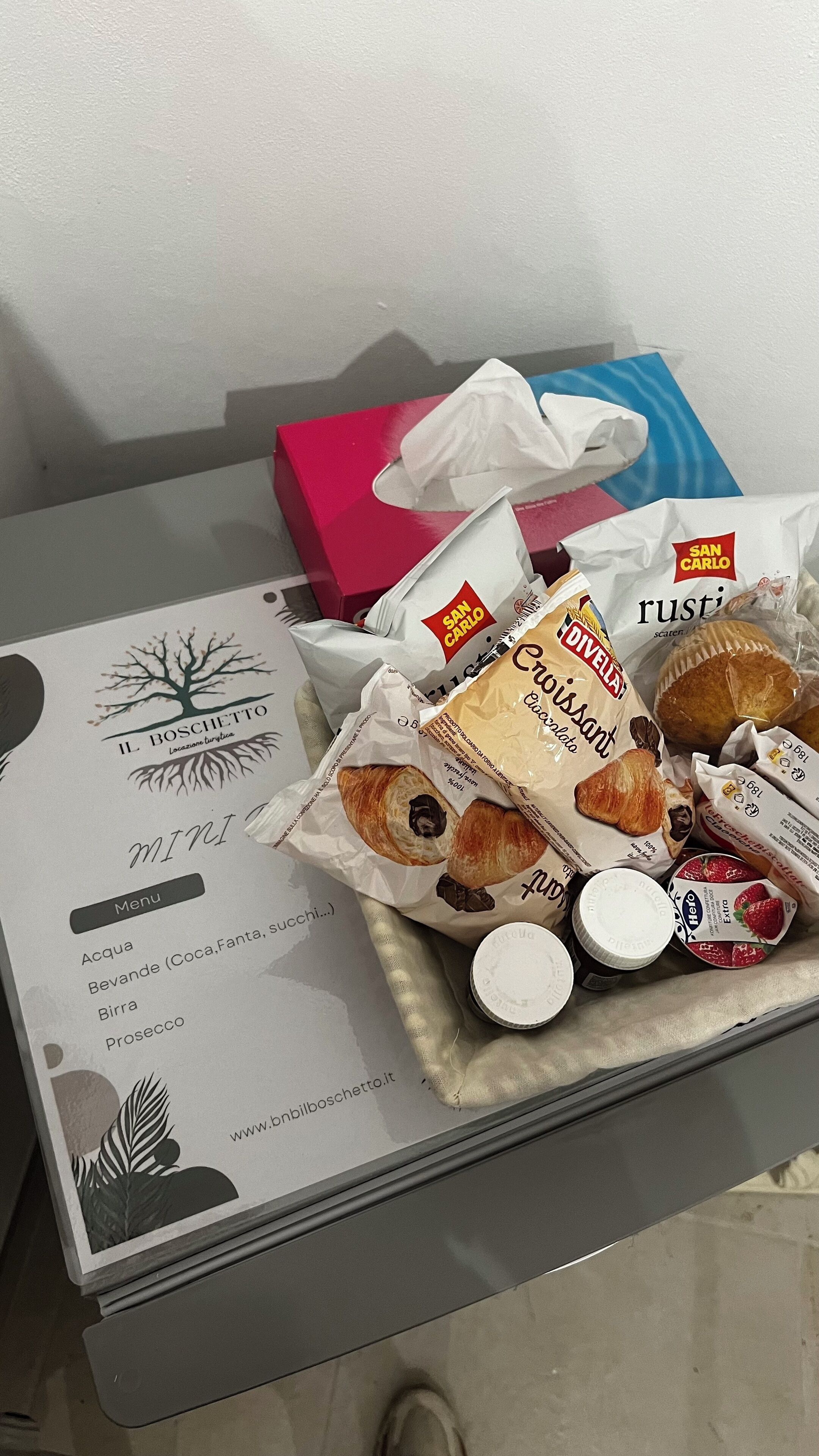 A table with a menu, a tissue box, and various food items including croissants and packaged goods.