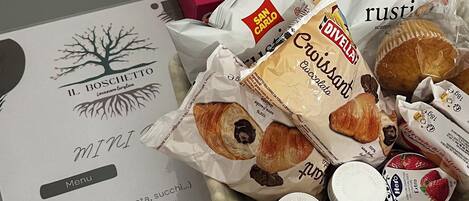 A table with a menu, a tissue box, and various food items including croissants and packaged goods.