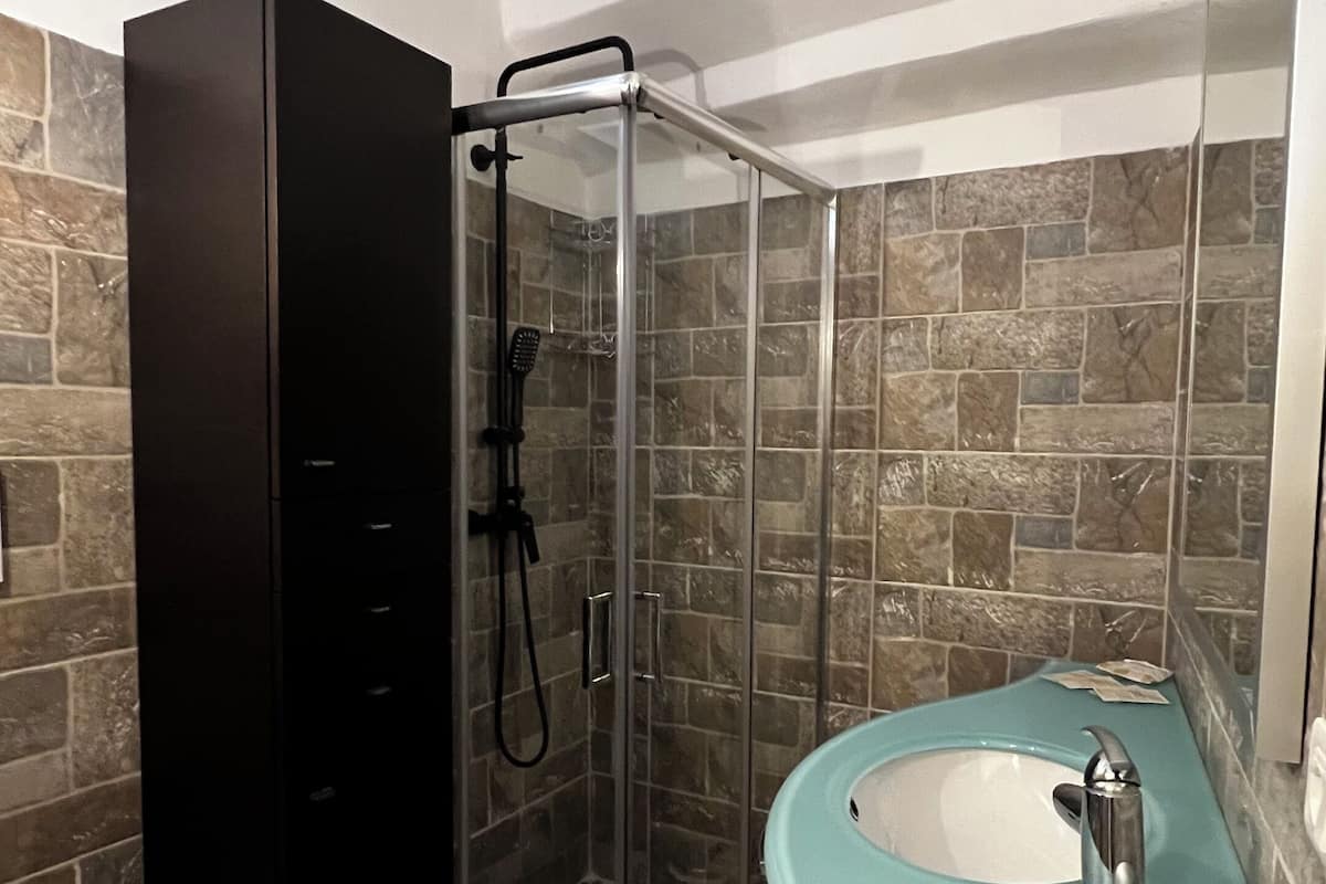 Un baño con ducha envuelta en vidrio, un armario negro, un inodoro blanco y un lavabo turquesa.