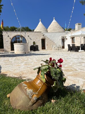 A stone building with a tiled patio, outdoor seating, and a flower pot with red flowers. - Locazione turistica Il Boschetto (Martina Franca)