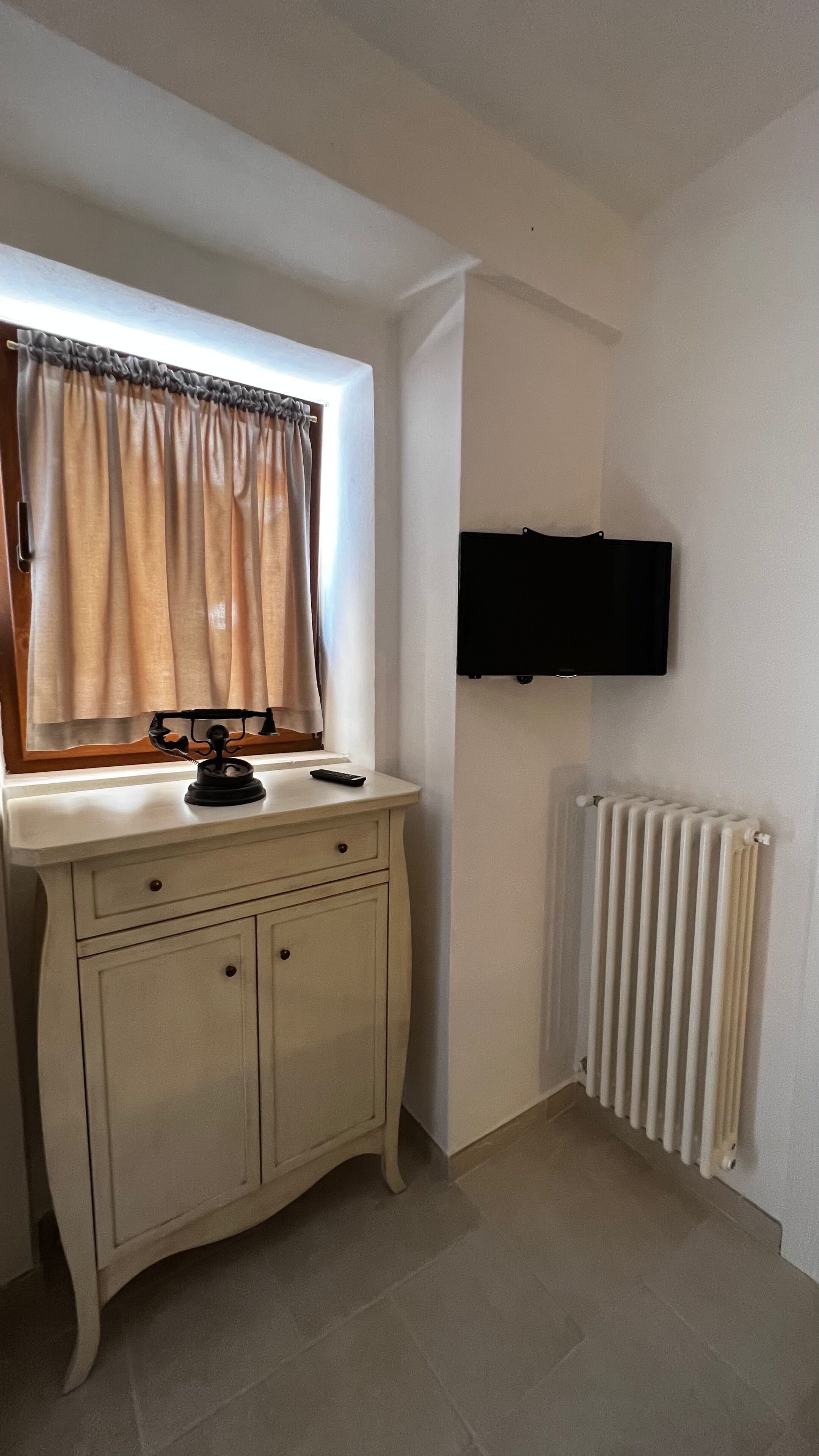 Ein Zimmer mit einem weißen Schrank, einem fenster mit Vorhängen, einem flachbildfernseher an der Wand und einem Heizkörper.