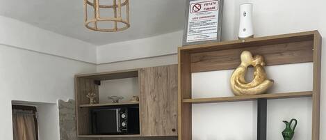 A modern kitchen with a wooden table, shelves with kitchenware, a hanging light fixture, and a stone wall backsplash.