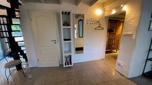 Un couloir avec une porte blanche, une chaise en métal, un mur blanc orné d’une enseigne suspendue et une porte en bois.