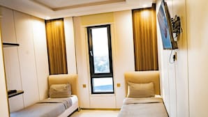 Un dormitorio acogedor con dos camas individuales, un televisor en la pared y una ventana con vistas a la ciudad.