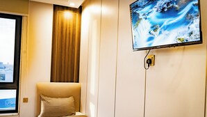 Una habitación de hotel con cama, ventana, televisor montado en la pared y cortina.