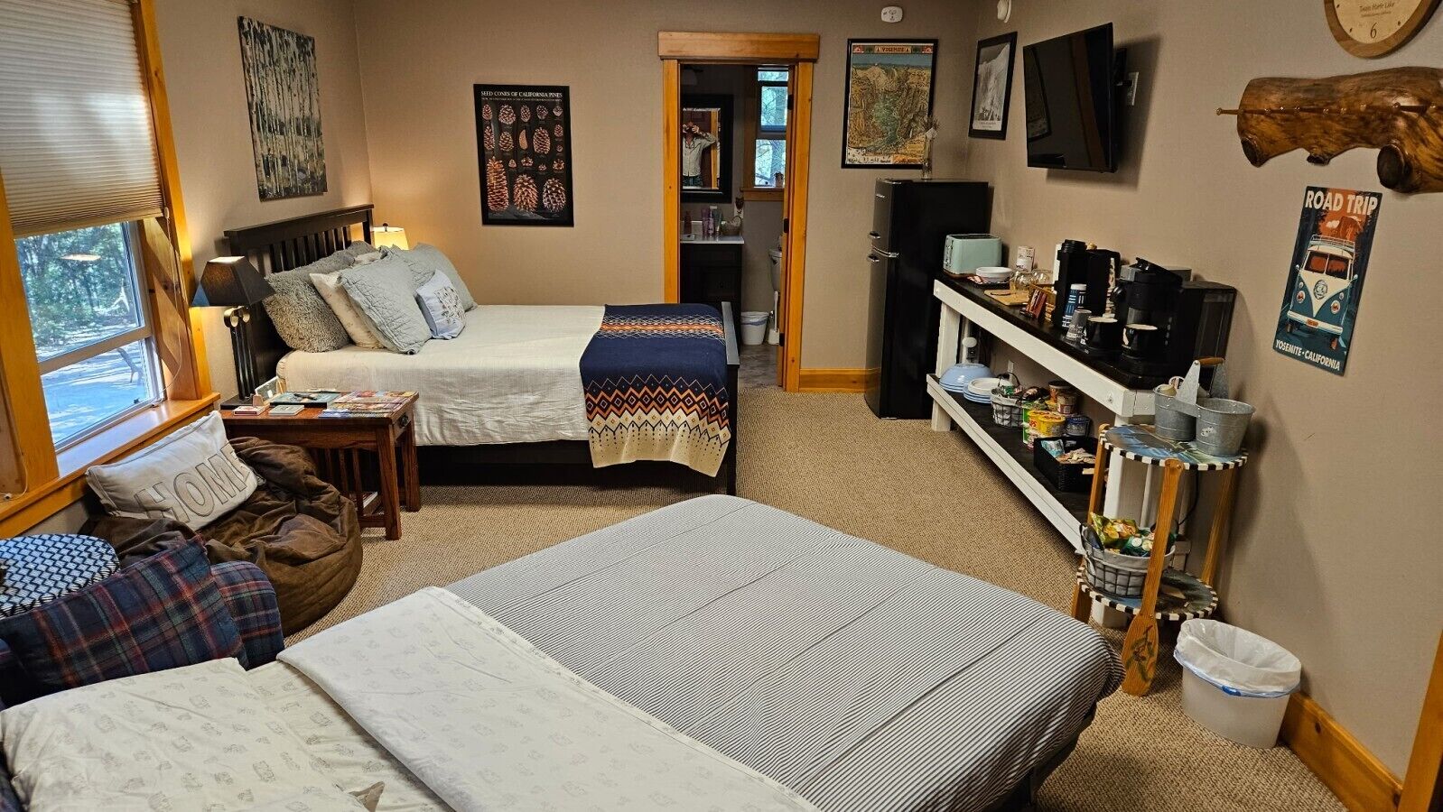 Een gezellige kamer met twee bedden, een klein tafeltje, een plank met diverse spullen en een raam met jaloezieën.