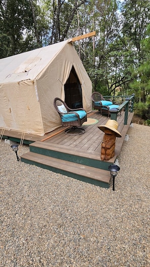 Een tent met een veranda, twee rieten stoelen, een houten bank en een lantaarn.
