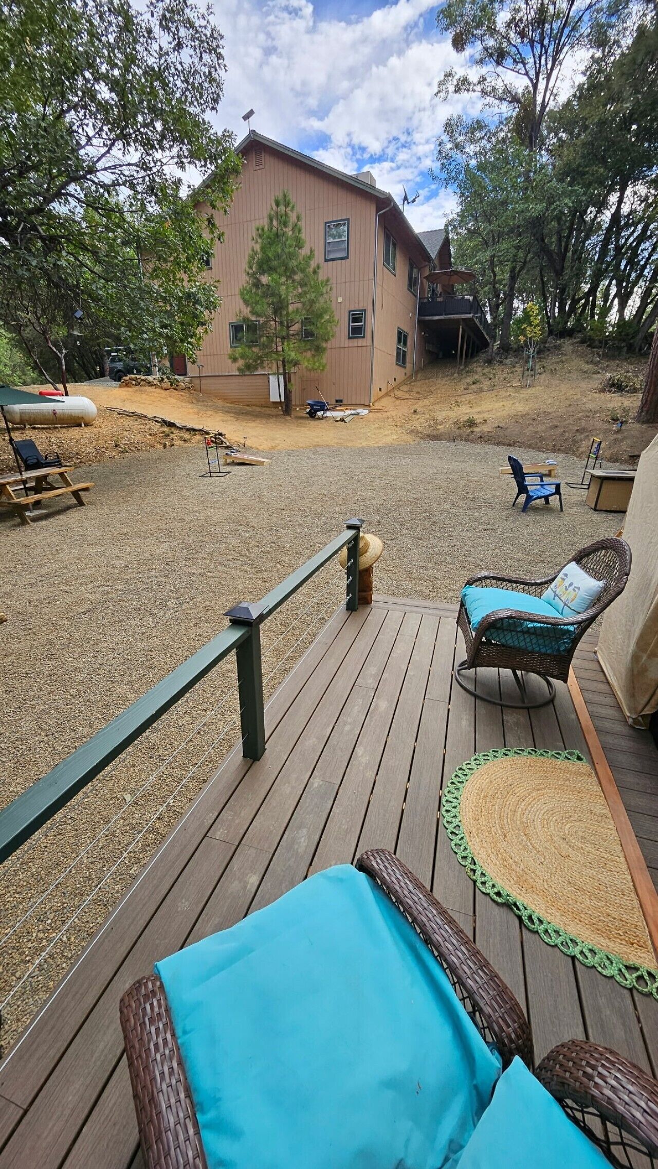 A wooden deck with outdoor furniture, a building in the background, and a gravel area.