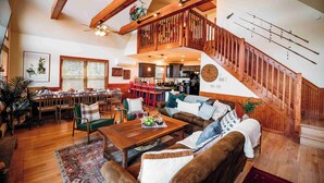 A spacious living room with a wooden staircase, a dining area, and a kitchen.