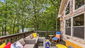 A deck with outdoor furniture, a stone wall, and a view of trees.