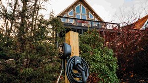 An electric vehicle charging station in a wooded area with a cabin in the background.