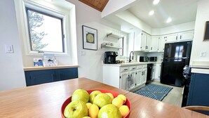 Una cocina moderna con armarios blancos, un refrigerador negro y un tazón rojo de fruta sobre la mesa.
