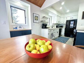 Una cocina moderna con armarios blancos, un refrigerador negro y un tazón rojo de fruta sobre la mesa.