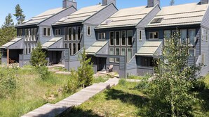 Una hilera de casas modernas, grises, con techos pronunciados y ventanas amplias, conectadas por una terraza de madera.