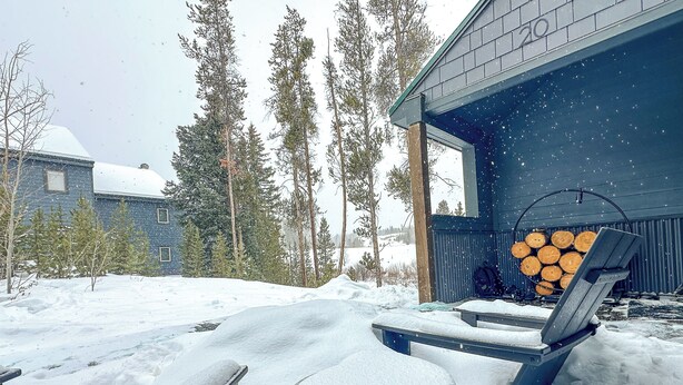 Un espacio al aire libre cubierto de nieve con una mesa y sillas, una pila de leña y un edificio con el número '20' en su fachada.