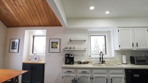 Una cocina con armarios blancos, una cafetera, un lavamanos y un ventanal.