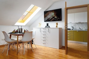 A modern kitchen with a skylight, a dining area with white chairs, and a television above the counter. - Golden River Apartment (Hlavní mesto Praha)
