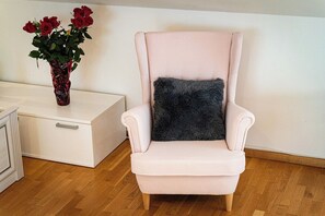 A chair with a fluffy pillow and a vase with red flowers on a white dresser. - Golden River Apartment (Hlavní mesto Praha)