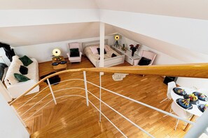 A modern loft bedroom with a wooden floor, a white bed, a desk, and a dining area with a table set for four. - Golden River Apartment (Hlavní mesto Praha)