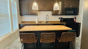 A kitchen with dark wooden cabinets, a granite countertop, a built-in microwave, and a large island with three wicker chairs. - Charming 3-bedroom house in historic grandview neighborhoods  (Dubuque)