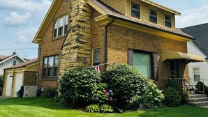 A two-story house with a stone chimney, a front porch with a bench, and a well-maintained lawn. - Charming 3-bedroom house in historic grandview neighborhoods  (Dubuque)