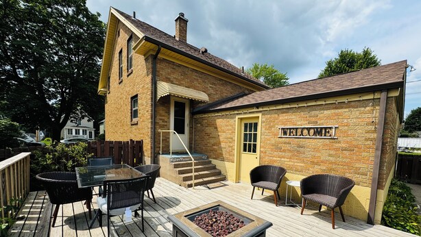 A wooden deck with a fire pit, outdoor furniture, and a 'WELCOME' sign on a brick building. - Charming 3-bedroom house in historic grandview neighborhoods  (Dubuque)